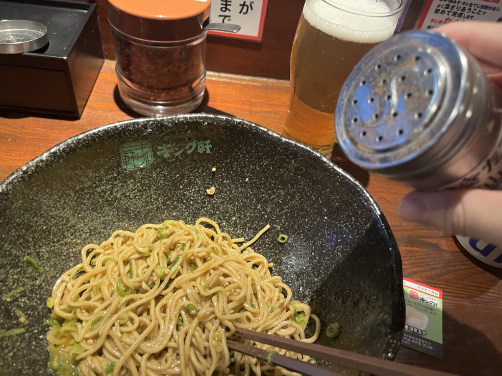 広島 キング軒の汁なし担々麺に追い山椒をしている写真